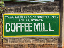 At the Othaya cooperative dry mill, a colorful green and yellow sign reads, "Othaya Farmers Co-op Society Limited - Coffee Mill".