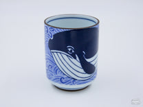 The Sad Whale Ceramic Cup is adorned with indigo blue whales swimming through water.